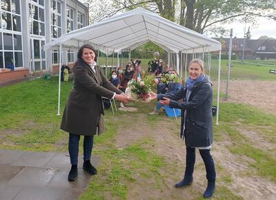 Bild vergr&ouml;&szlig;ern: Schulverbandsvorsteherin Martina Falkenberg &uuml;berreicht der frisch gew&auml;hlten neuen Schulleiterin vor dem Hintergrund des Gremiums zur Schulleitungswahl einen Blumenstrau&szlig; als herzlichen Willkommensgru&szlig;